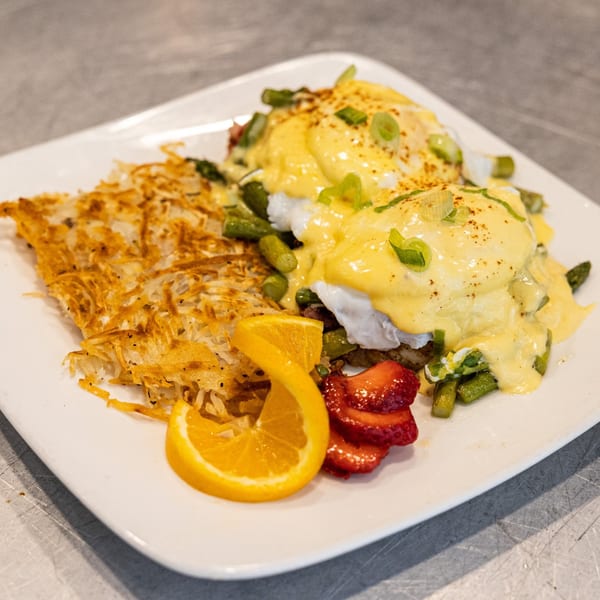 5 Spot's Eggs Benedict with hash browns, asparagus, orange slice, and strawberries on a white plate.