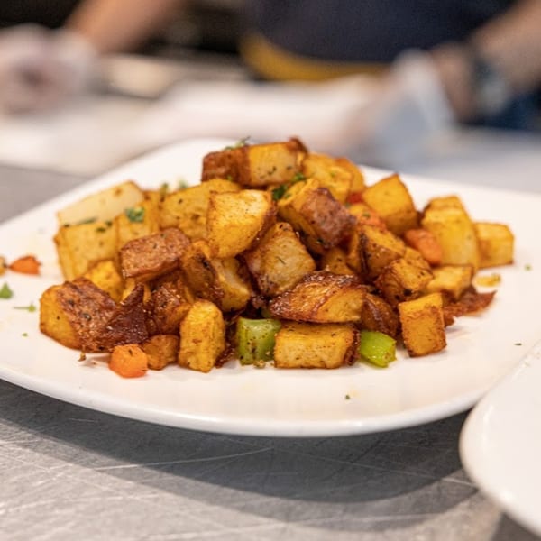 A white plate piled high with crispy, golden-brown breakfast potatoes, garnished with herbs and diced vegetables.