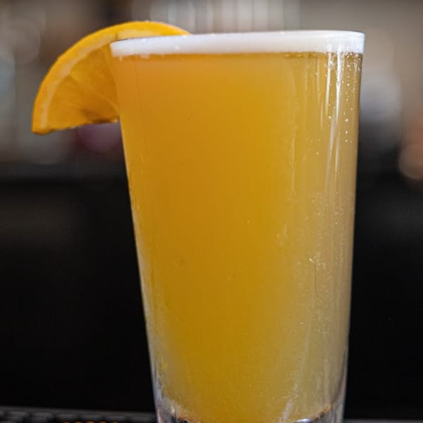 A glass of mimosa with an orange slice on the rim, served at 5 Spot.