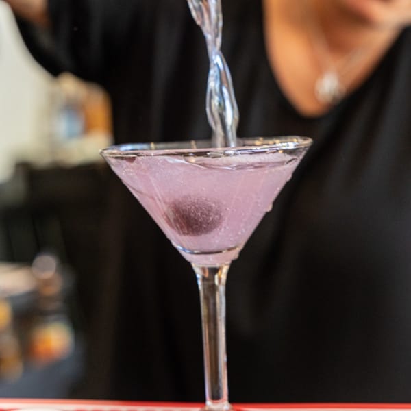 A bartender pours a purple cocktail with a single cherry into a martini glass at 5 Spot.