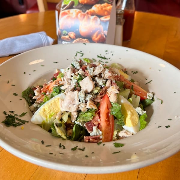 A Cobb salad with chicken, bacon, blue cheese, tomato, and hard-boiled egg in a white bowl.