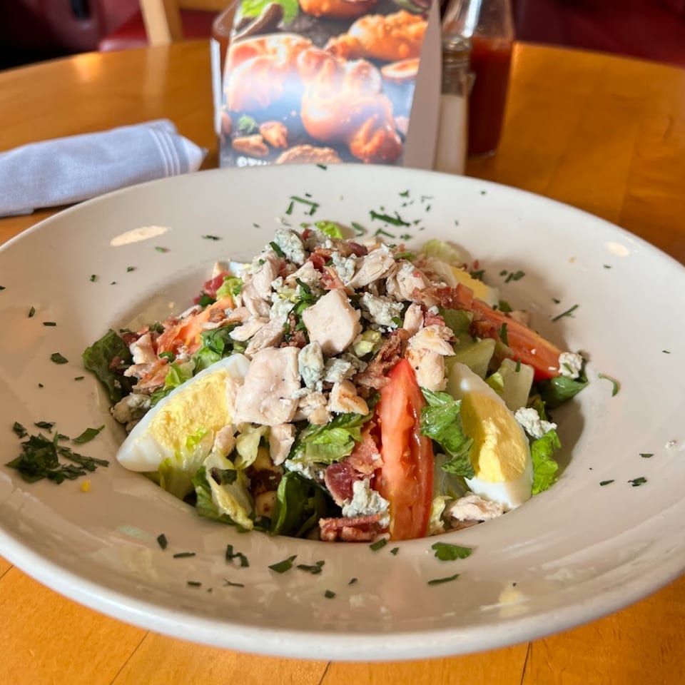 A Cobb salad with chicken, bacon, blue cheese, tomato, and hard-boiled egg in a white bowl.
