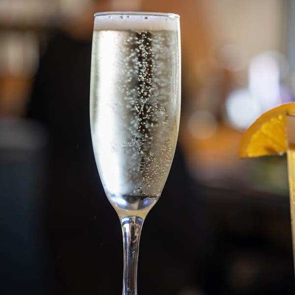 A champagne flute filled with sparkling mimosa, garnished with an orange slice, at 5 Spot.